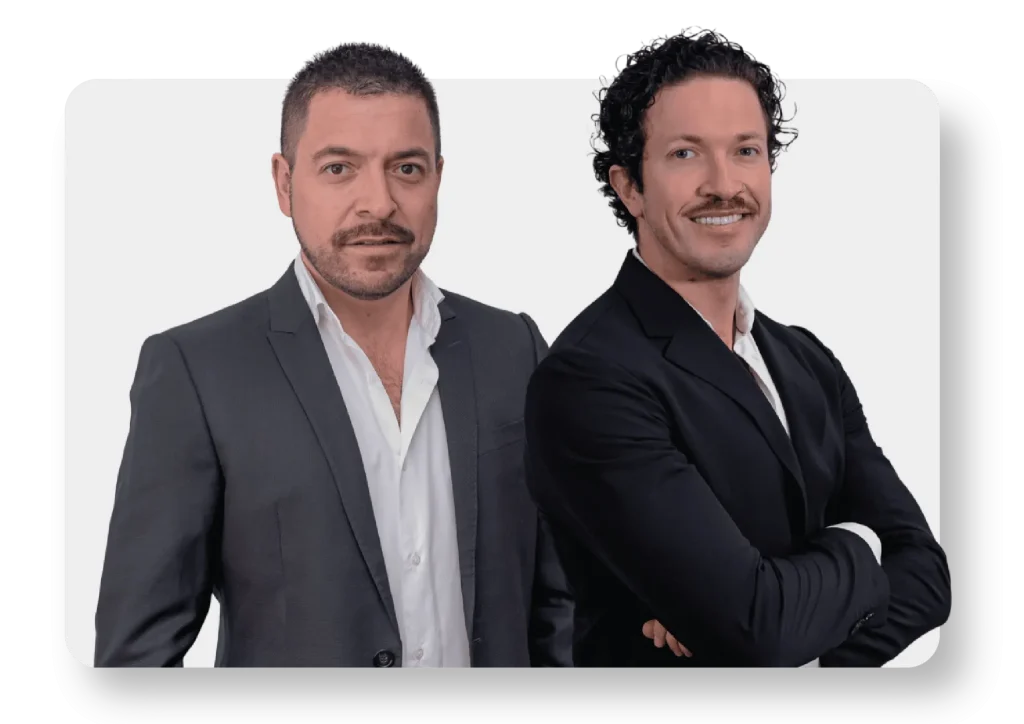 Retrato Nicolás Orbenes y Julio Orbenes, fundadores de NOMII, con traje formal, sobre fondo blanco.
